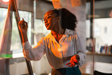 Businesswoman in conference room. Young African businesswoman making a business plan. Woman writing on the glass board in office.