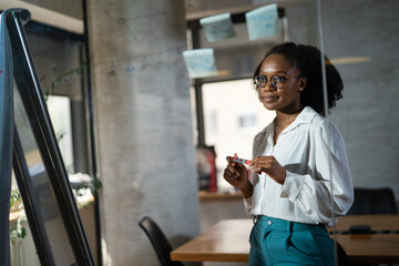 Businesswoman in conference room. Young African businesswoman making a business plan. Woman writing on the glass board in office.