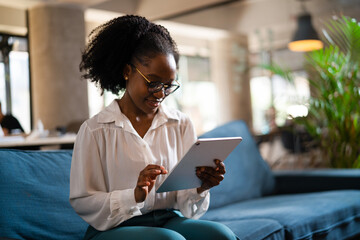 Beautiful African businesswoman sitting on sofa in office. Young woman using digital tablet.