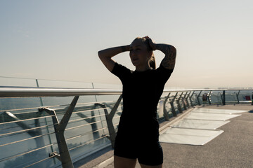 Fototapeta premium Fitness young sportswoman girl in the morning doing warm-up exercises before training on the street in the city on the bridge Sport health