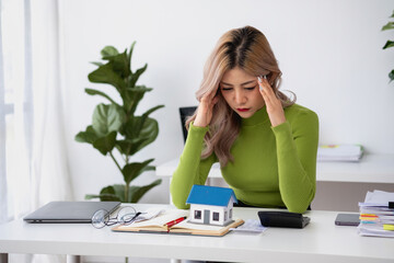 oung Asian woman sitting and calculating expenses and mortgage with calculator and house on table...