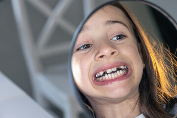 Caucasian preteen girl with braces on her teeth looking at the mirror.