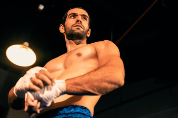 Caucasian boxer portrait with muscular and athletic body wrapping his hand or fist on the ring be...