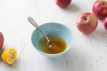 A bowl of honey and lemon juice surrounded by fresh apples on a light blue background. Stage of cooking delicious fruit pie or other dessert