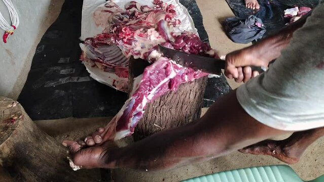 The butcher is cutting large pieces of meat into smaller pieces on a wooden block