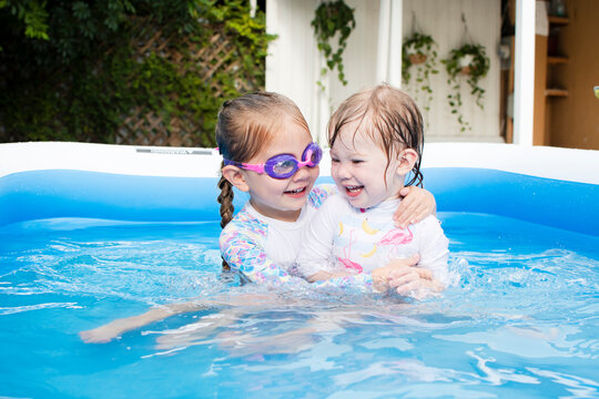 Cute Caucasian sisters playing and hugging in swimming pool