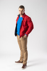 A man of athletic build in a red jacket stands and holds his hands in his pockets