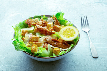 Caesar salad with chicken breast, lettuce, croutons, and a lemon, on a slate background, with a fork