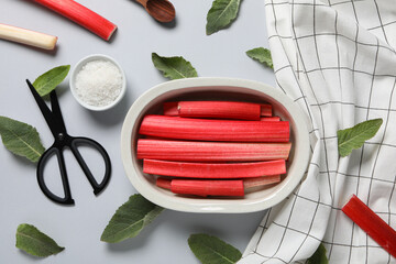 Rhubarb stalk in bowl, mint, salt, scissors and white checkered towel on gray background, flat lay
