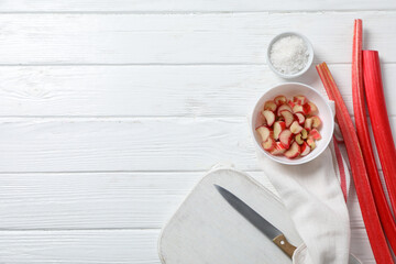 Knife on the board, rhubarb, bowls with salt and chopped rhubarb on white wooden background, space for text