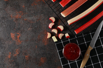 Jam jar and knife on black towel, sliced rhubarb on dark background, space for text