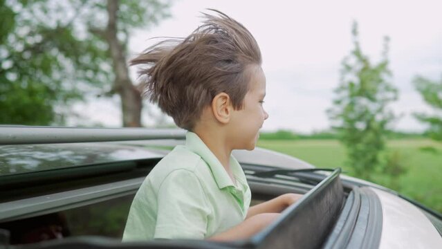 Funny happy little boy stands in open car sunroof during trip, summer. Childhood