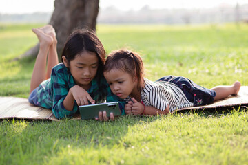 Two young girls lying on the lawn looking at their phones, summer, golden hour, sunset. SSTKHome