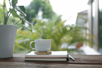 white coffee cup and books and pencils and pothos plant pot on brown wooden table