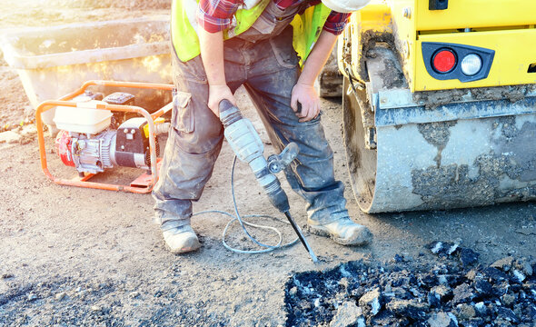 Builder breaking asphalt with electric breaker