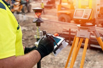 Site engineer surveyor using rugged tablet controller computer to operate EDM total station for...