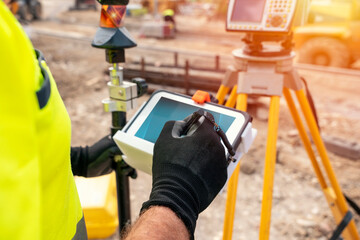 Site engineer surveyor using rugged tablet controller computer to operate EDM total station for...