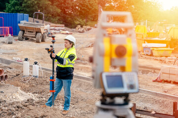 Female site engineer surveyor working with theodolite total station EDM equipment on a building construction site outdoors