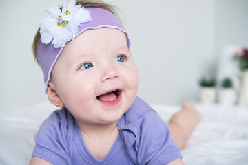close up baby with blue eyes wearing a purple outfit smiling lying on bed