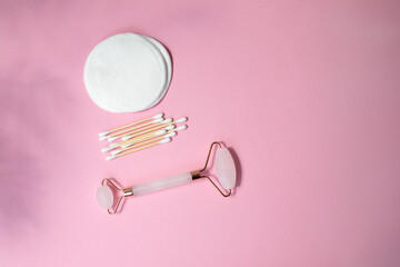 Set of eco friendly devices. Pink quartz facial massage roller, ear sticks and reusable cotton pads on a pink background. Flat lay