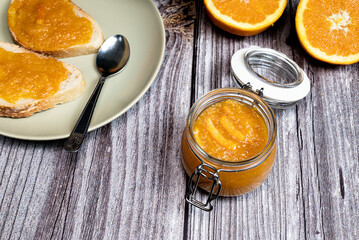Delicious homemade orange marmalade in a glass jar. Top view of plate with slices of with homemade jam on white wooden table.