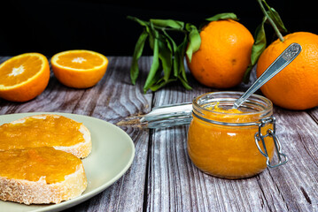 Delicious homemade orange marmalade in a glass jar. Jam on slice of bread on a plate. Horizontal photo with black background.