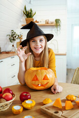 Happy Halloween! Cute laughing girl in witch hat with a pumpkin. Scary face on jack-o-lantern to...