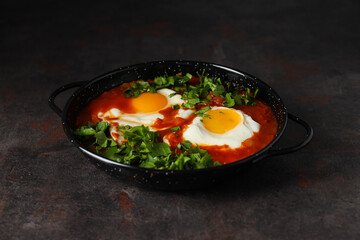 Shakshuka in frying pan on dark background