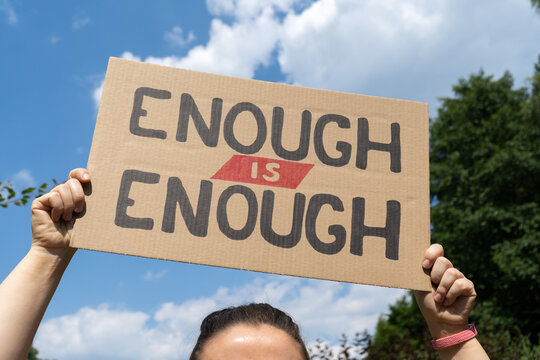 Woman holding placard sign with text Enough is enough. Female protestor with cardboard banner at protest rally demonstration. Call for change, demand action on the social justice matter.