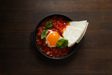Shakshuka in pan and pita on wooden background, top view