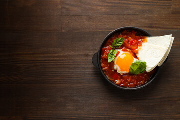 Shakshuka in pan and pita on wooden background, space for text