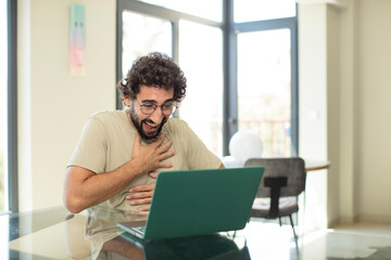 young adult bearded man with a laptop laughing out loud at some hilarious joke, feeling happy and cheerful, having fun