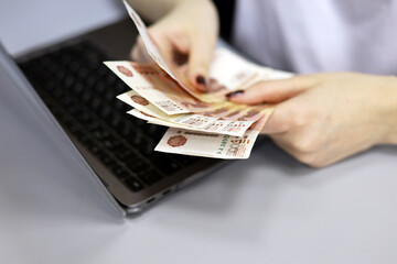 Russian rubles in female hands, cash pay, salary, inflation or savings concept. Woman counting money at laptop