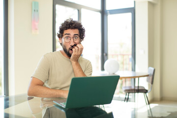 young adult bearded man with a laptop feeling terrified, in horror and panic