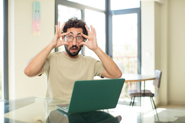 young adult bearded man with a laptop keeping an eye on you, not trusting, watching and staying alert and vigilant