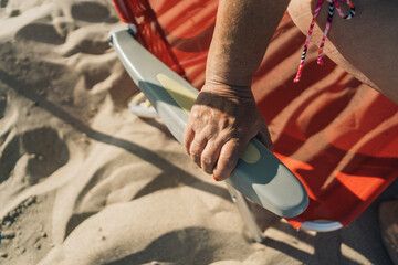 Hand of retired senior woman on vacation sitting on a beach chair. Close-up image of an older...