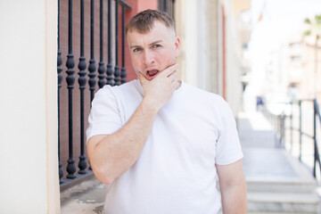 handsome man with mouth and eyes wide open and hand on chin, feeling unpleasantly shocked, saying...