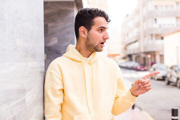 Obraz premium young hispanic man feeling shocked and surprised, pointing and looking upwards in awe with amazed, open-mouthed look