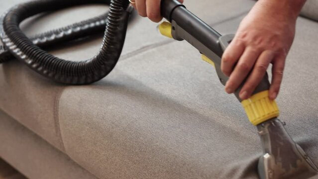 Dry cleaner's man employee removing dirt from furniture in flat, closeup, vacuum clean sofa with professional equipment. cleaning sofa with washing suction cleaner closeup.
