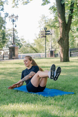 Fototapeta premium portrait of a young sporty girl doing abdominal exercises on a sports mat outdoors while exercising in the park healthy lifestyle concept