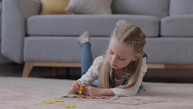 Educational toys for children. Cute little girl making a wooden puzzle with colorful blocks lying on the carpet at home. Brain teasers toy for motor development and logical thinking. Home leisure.