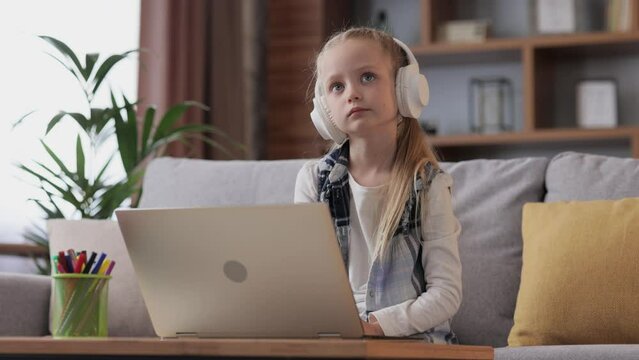 Cute primary school girl studying at home using laptop computer. Serious child doing homework, answering online test question, passing the exam. Distance learning. Children home education.