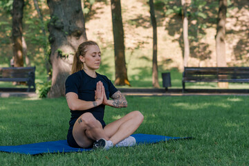 Fototapeta premium portrait of young sporty girl meditating doing yoga on sports mat outdoors while exercising in park healthy lifestyle concept