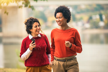 Two smiling young women friends jogging outside in the forest next to the lake in red sweatshirts