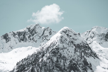 Mountain peaks covered with snow and a small cloud above them in a light blue sky. Swiss Alps.