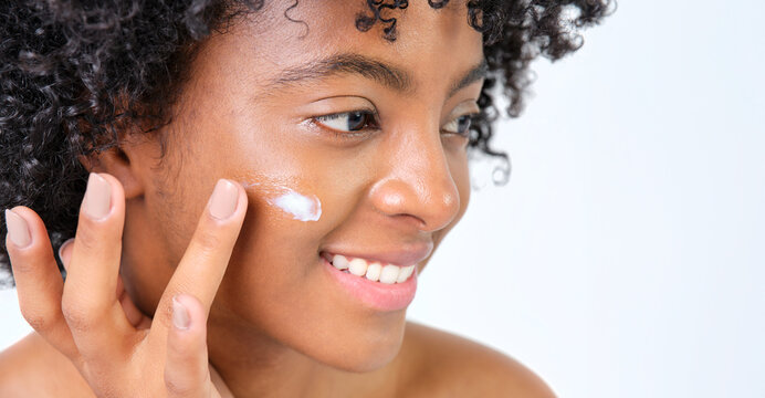 Young African American Girl Smiling In Profile Giving Cream To Her Face On White Background