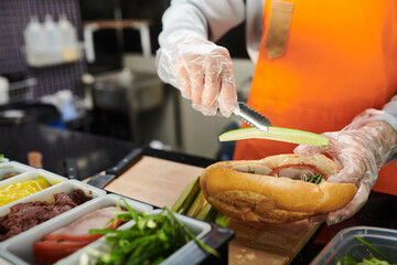 Cook putting cucumber slice in cut traditional Vietnamese bread called banh mi