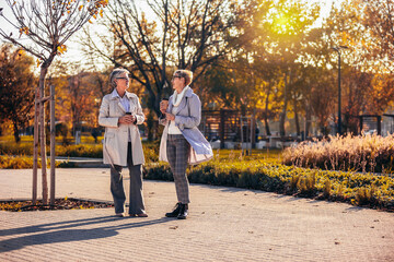 Fototapeta premium Two women drinking coffee and walking in the park