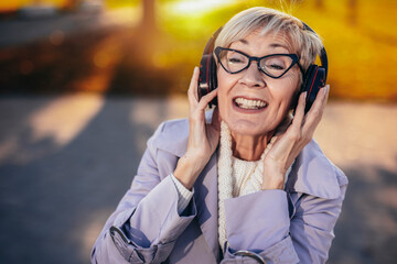 An older woman listening to music in the colorful park in the autumn