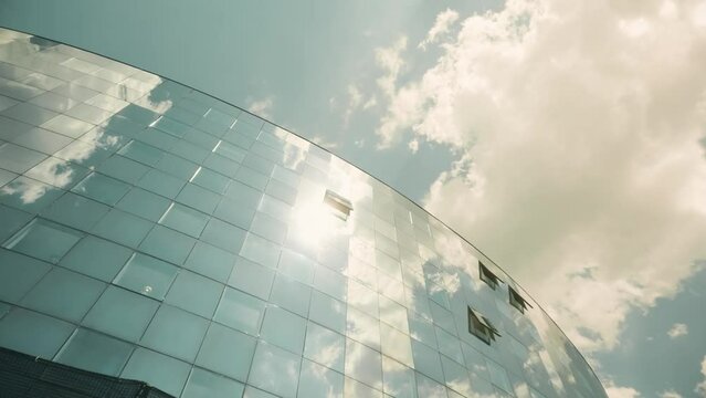 Modern glass facade of an office building with open windows reflects sun, sky and clouds. Business opportunity concept
